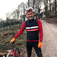 Keen employee in cycling gear smiling standing next to a bicycle